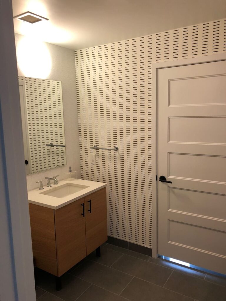 Professional wallpaper installation with a clean white and black vertical dash stripe geometric pattern covering the back wall of a modern bathroom, Costa Blanca Spain
