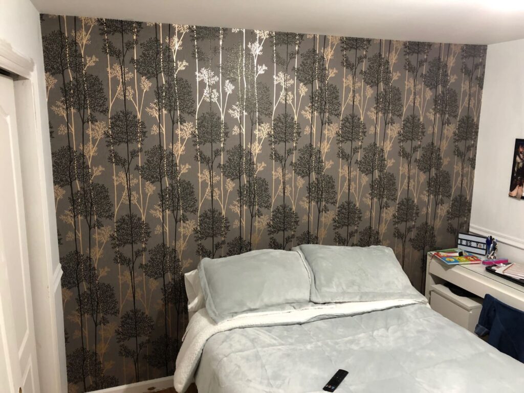 Professional bedroom feature wall wallpaper installation with a charcoal grey background and metallic gold and black birch tree pattern, Costa Blanca Spain
