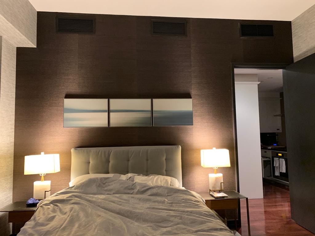 Professional grasscloth wallpaper installation with dark espresso brown woven texture as a bedroom headboard feature wall, with light grey grasscloth on side walls, Costa Blanca Spain