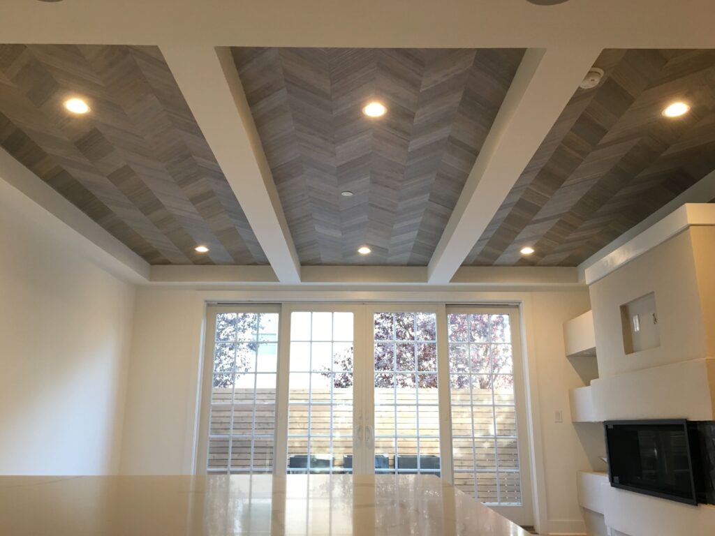Professional wallpaper installation on a coffered ceiling featuring a grey herringbone wood-effect pattern in a modern living room, Costa Blanca Spain