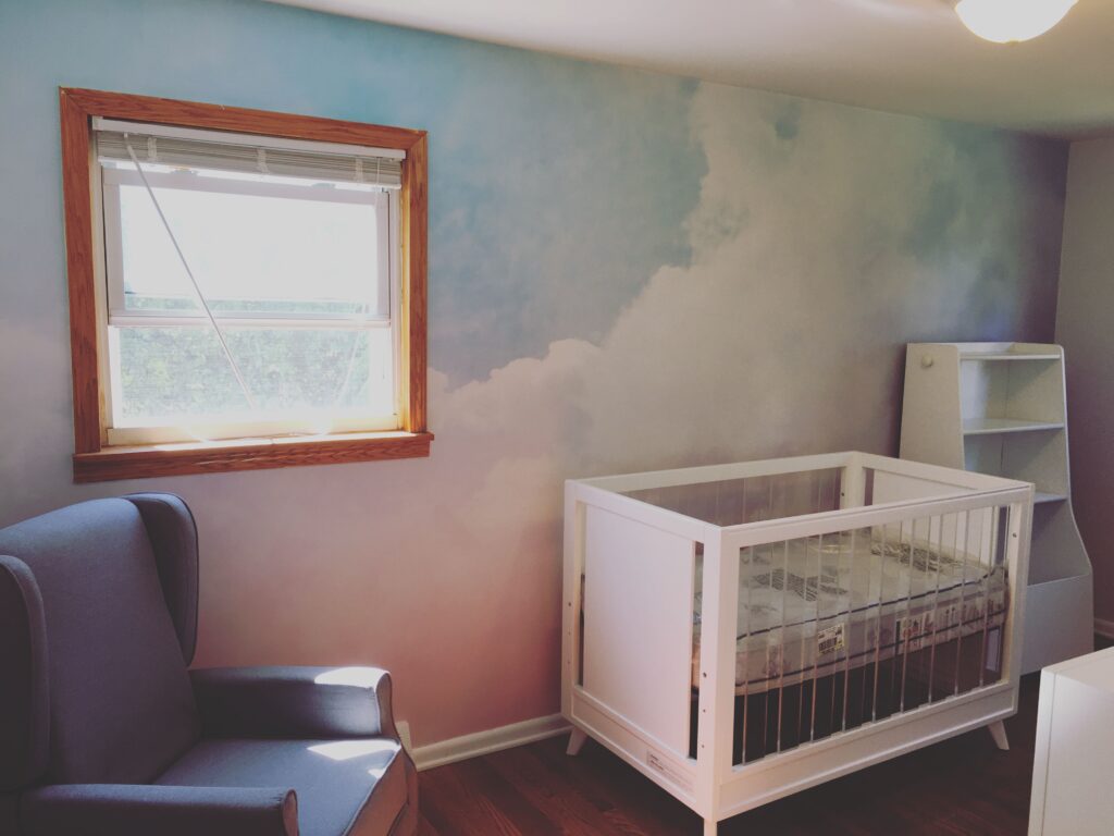 Professional full wall cloud mural wallpaper installation in a nursery with soft blue sky and watercolour clouds transitioning to lavender, Costa Blanca Spain