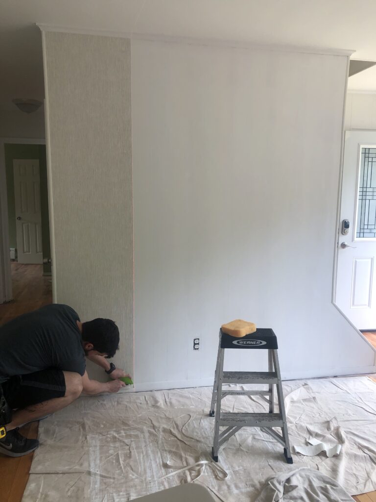Professional wallpaper installer carefully trimming the bottom edge of a subtle textured wallpaper panel at skirting board level in a living room, Costa Blanca Spain