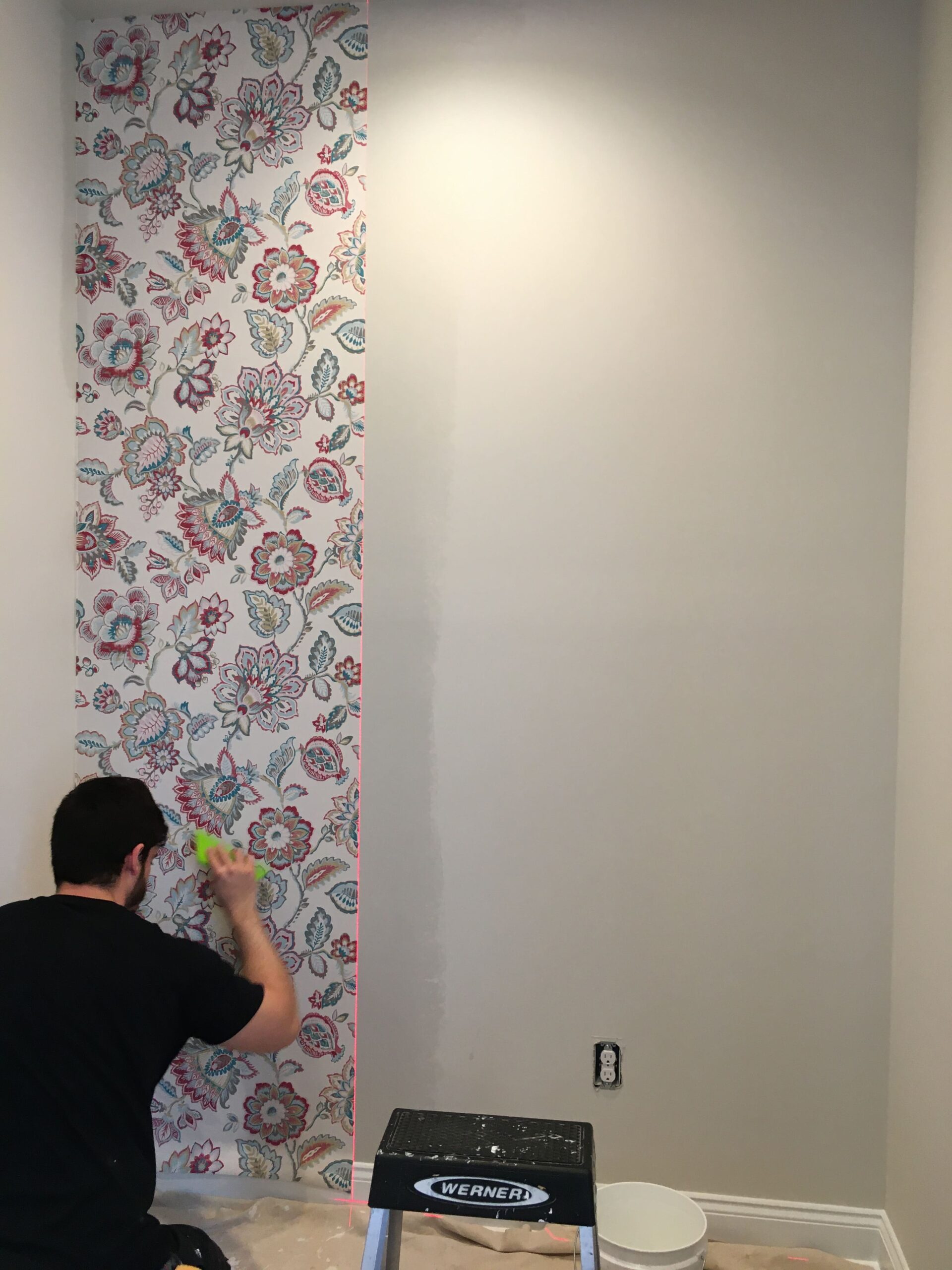Professional wallpaper installer carefully smoothing a large scale red and blue floral Jacobean pattern wallpaper panel during installation, Costa Blanca Spain