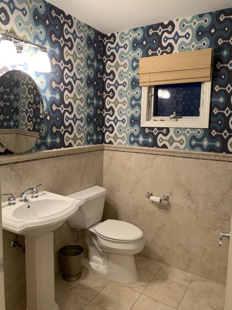 Professional wallpaper installation with a bold blue navy and teal ikat geometric pattern above marble effect tiles in a bathroom, Costa Blanca Spain