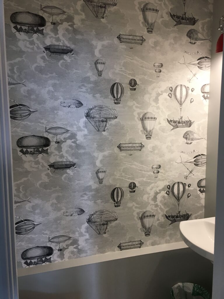 Professional wallpaper installation featuring a grey and white vintage steampunk hot air balloon and airship illustration pattern in a powder room, Costa Blanca Spain