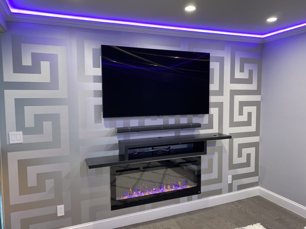 Professional wallpaper installation with a large scale grey and white Greek key geometric pattern on a media room feature wall with electric fireplace and LED lighting, Costa Blanca Spain