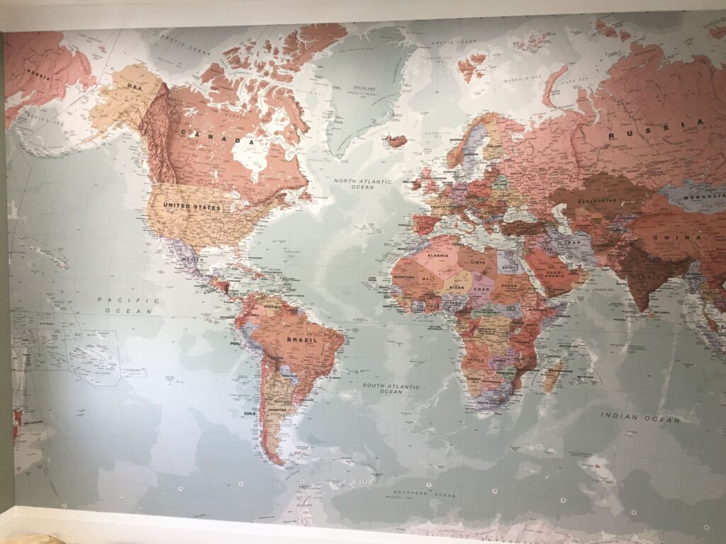 Professional full wall world map mural wallpaper installation in terracotta, blush and sage tones covering an entire wall, Costa Blanca Spain