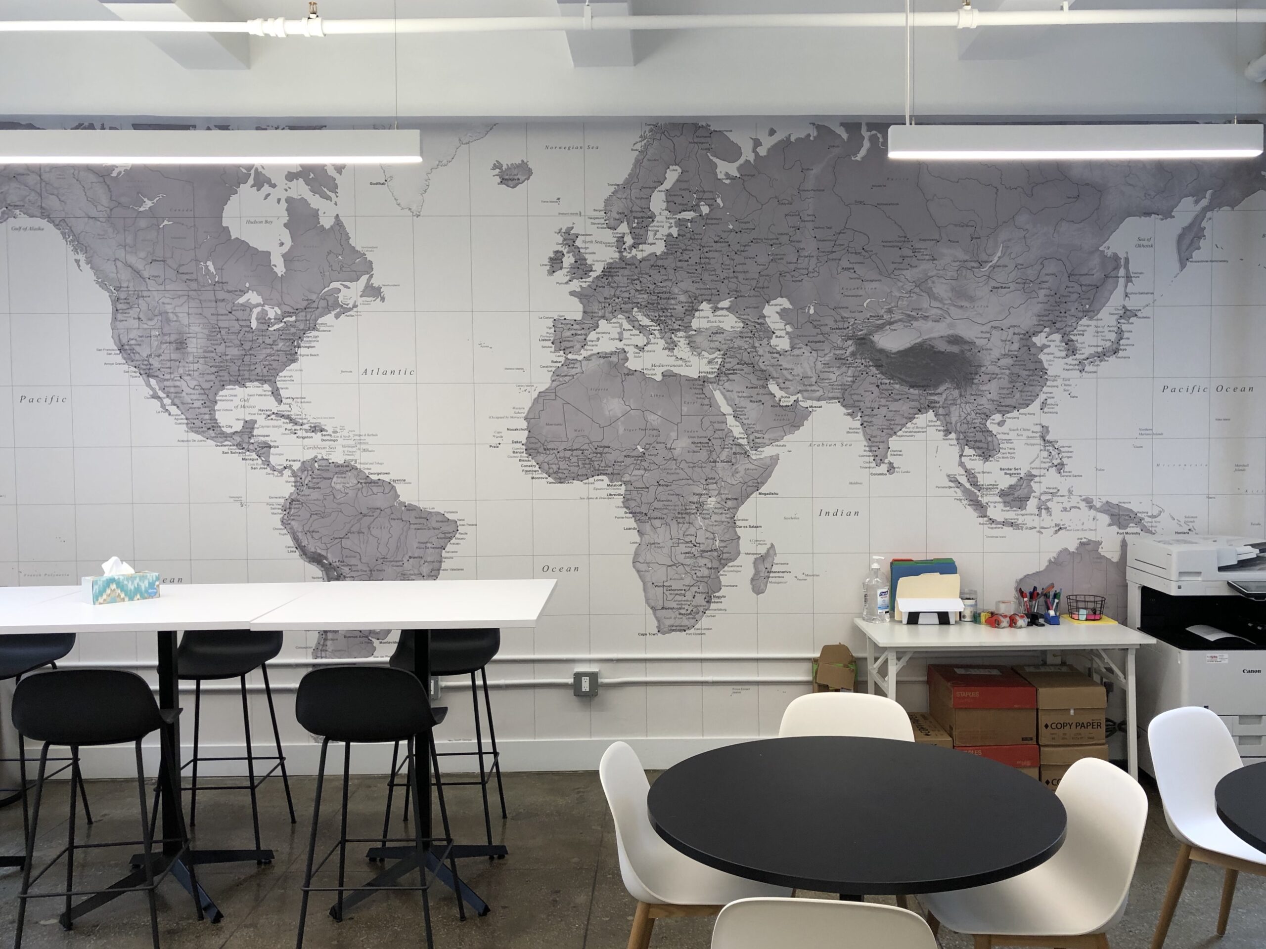 Professional large scale monochrome grey and white world map mural wallpaper installation covering a full wall in a modern commercial office breakout area, Costa Blanca Spain