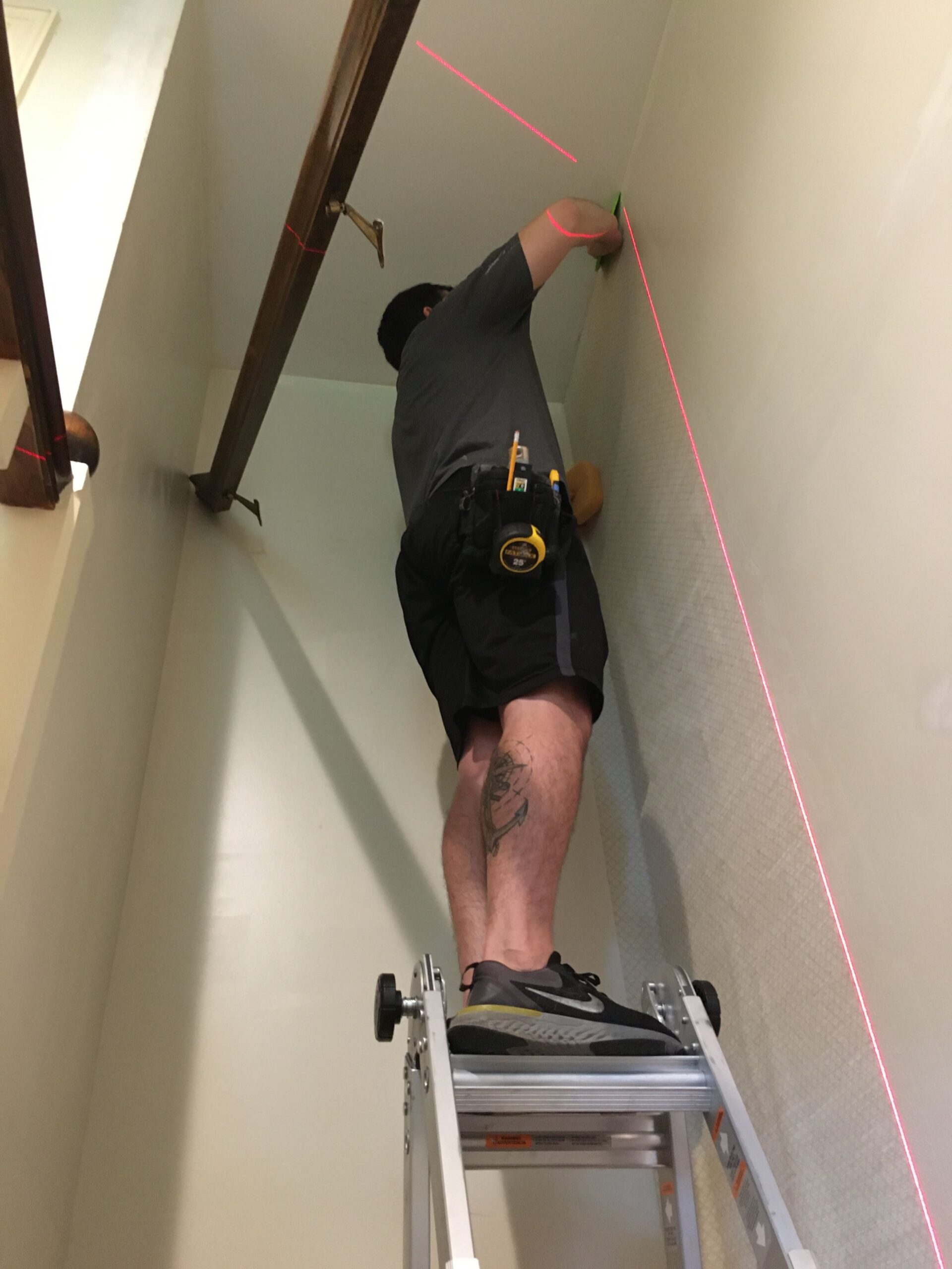 Professional wallpaper installer aligning wallpaper with a laser level while working on a ladder.