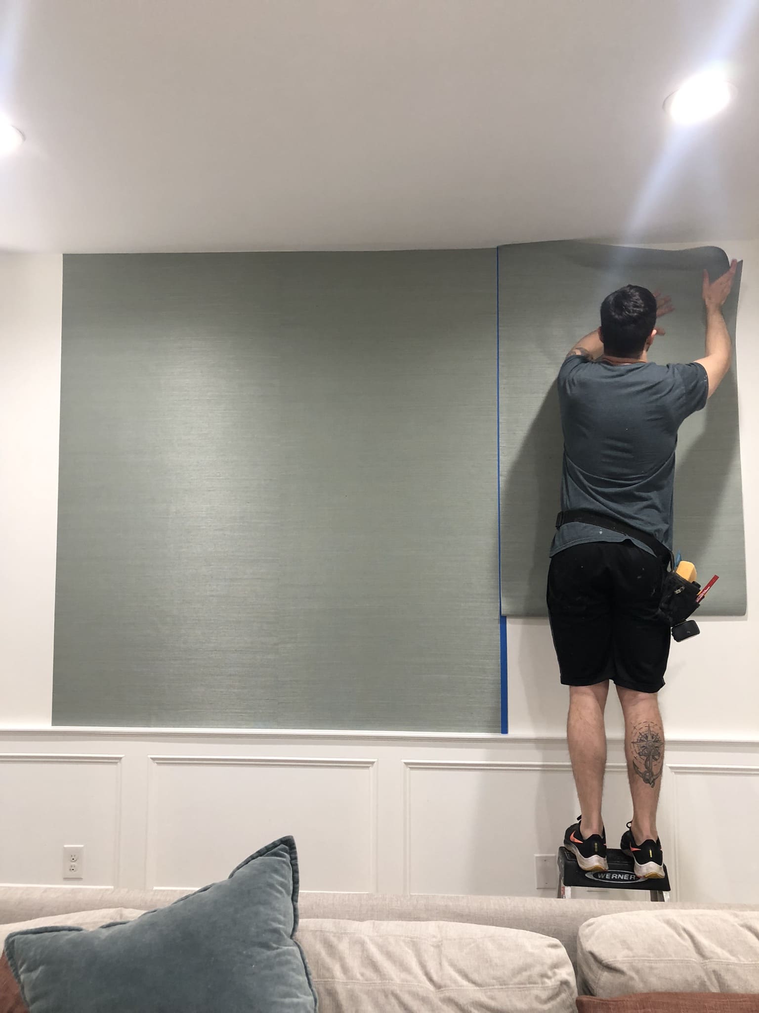 Wallpaper installer performing a double-cut on blue grasscloth wallpaper using protective tape for a seamless finish in Jávea, Spain